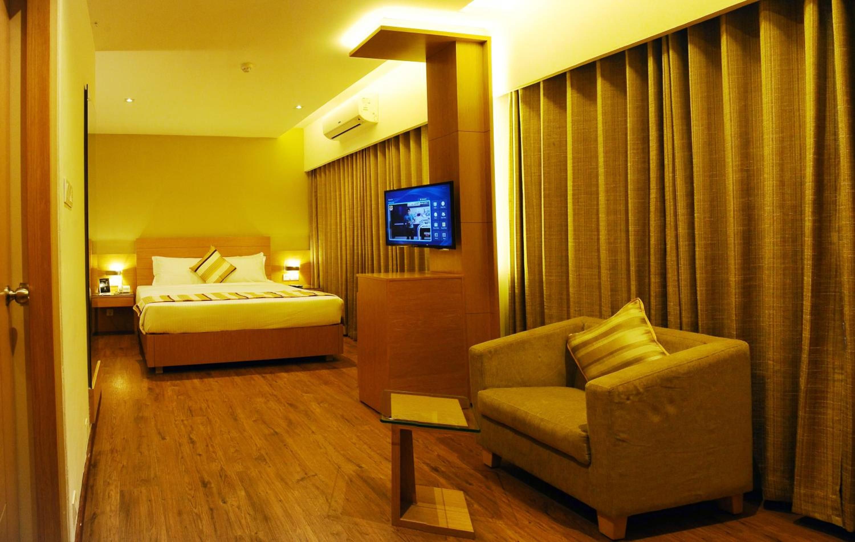 A hotel room with a bed, a sofa, a television, and curtains.