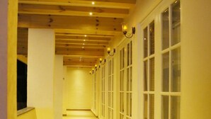 Un pasillo con vigas de madera, ventanas amplias y suelo de madera.