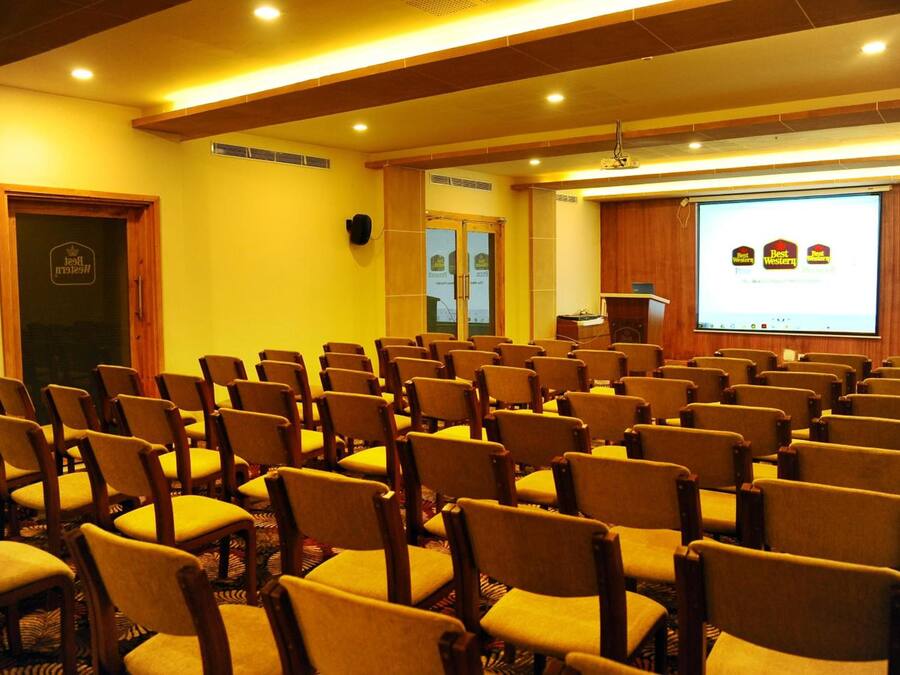 A conference room with rows of chairs, a podium, and a projection screen displaying a logo.