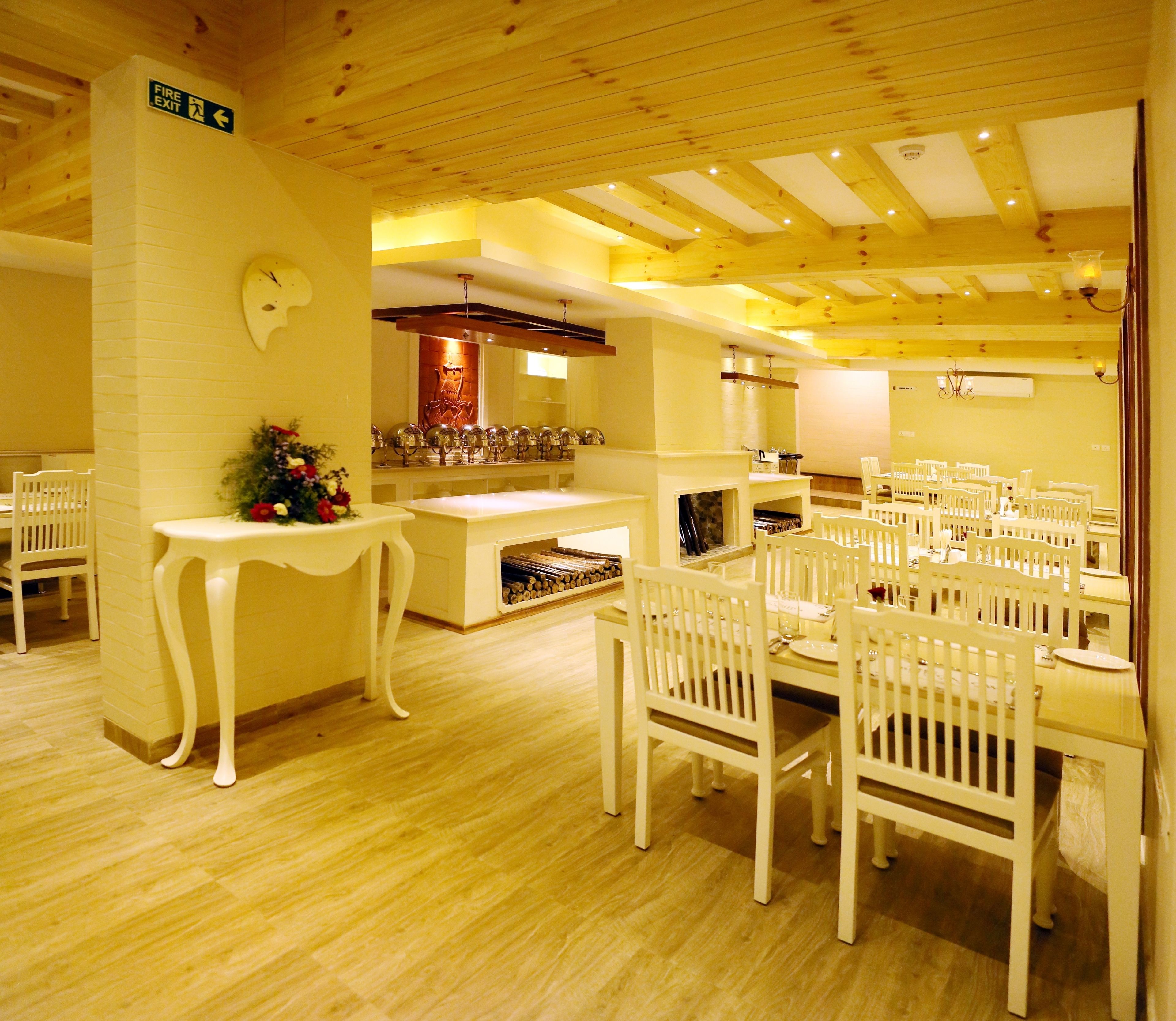 A dining area with white chairs and tables, a fireplace, and a fire exit sign.
