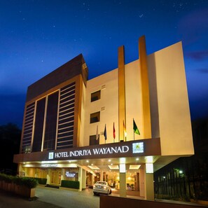 A hotel with a modern design, featuring a prominent entrance and multiple flags displayed outside. - Hotel Indriya Wayanad (Vythiri)
