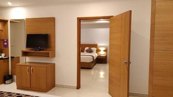 Habitación de hotel con cama, televisor montado en un mueble de madera, armario y una puerta que da a otra habitación.