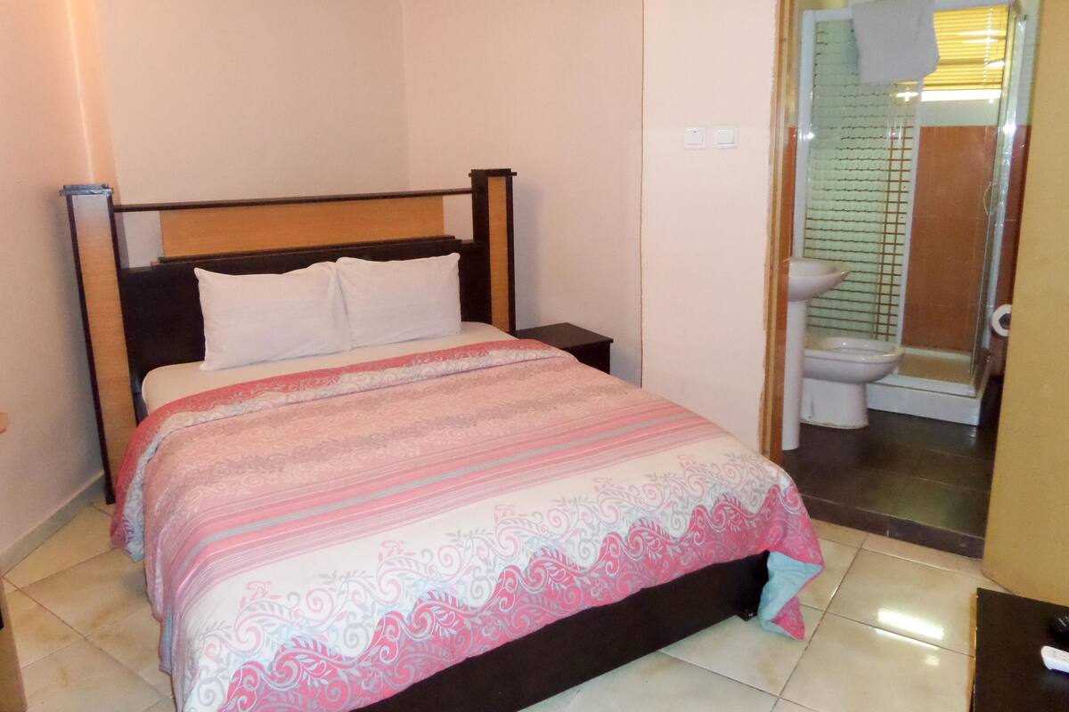 A hotel room with a bed, a nightstand, and a bathroom visible through an open door.
