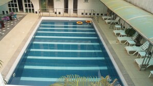 A swimming pool with clear blue water, surrounded by white lounge chairs and a covered seating area. - Royalview Hotel And Suites (Lagos)