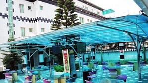 An outdoor seating area with blue chairs and tables, a glass canopy, and a building in the background. - Royalview Hotel And Suites (Lagos)