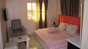 A bedroom with a bed, a chair, a desk, and a TV. - Royalview Hotel And Suites (Lagos)