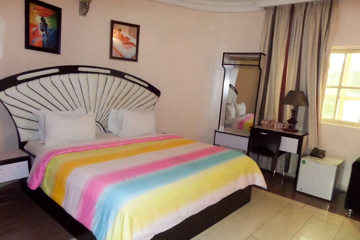 A bed with a rainbow-colored blanket, a black headboard, and a mirror above it.