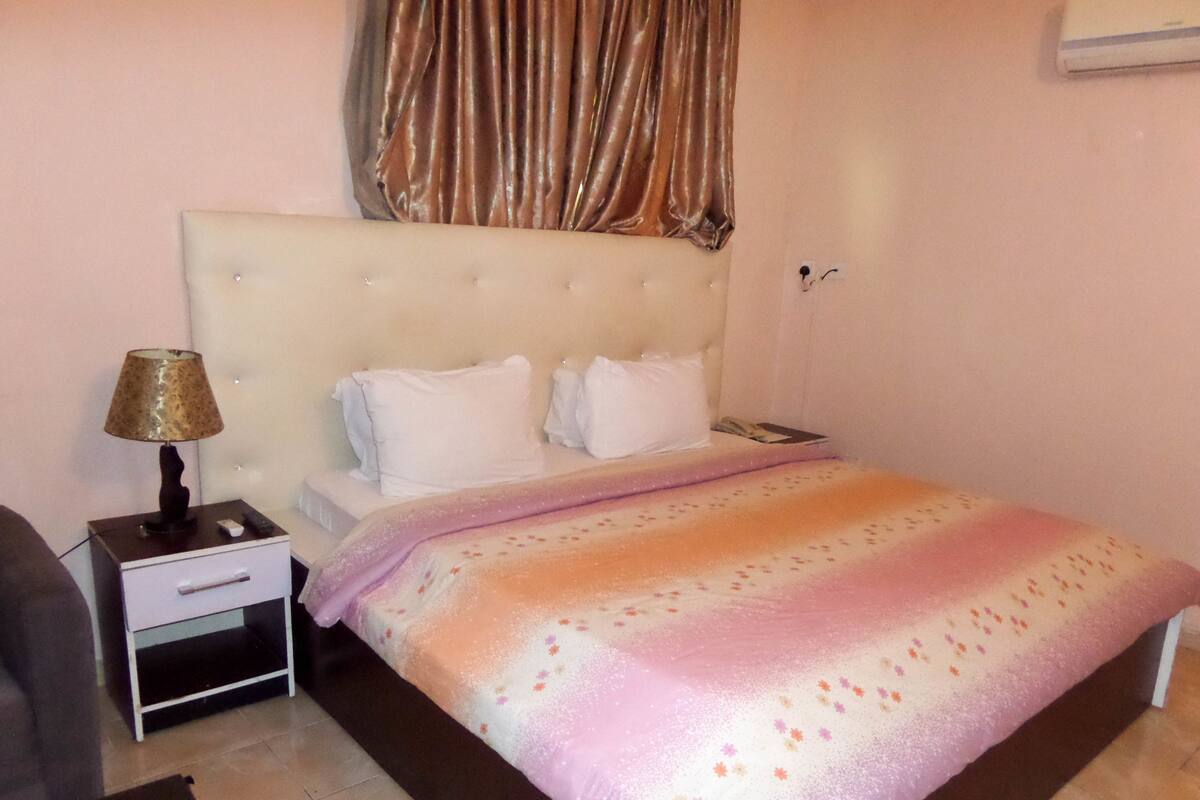 A bedroom with a bed, a nightstand, a lamp, and a curtain.