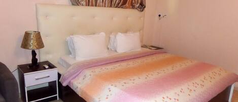A bedroom with a bed, a nightstand, a lamp, and a curtain.