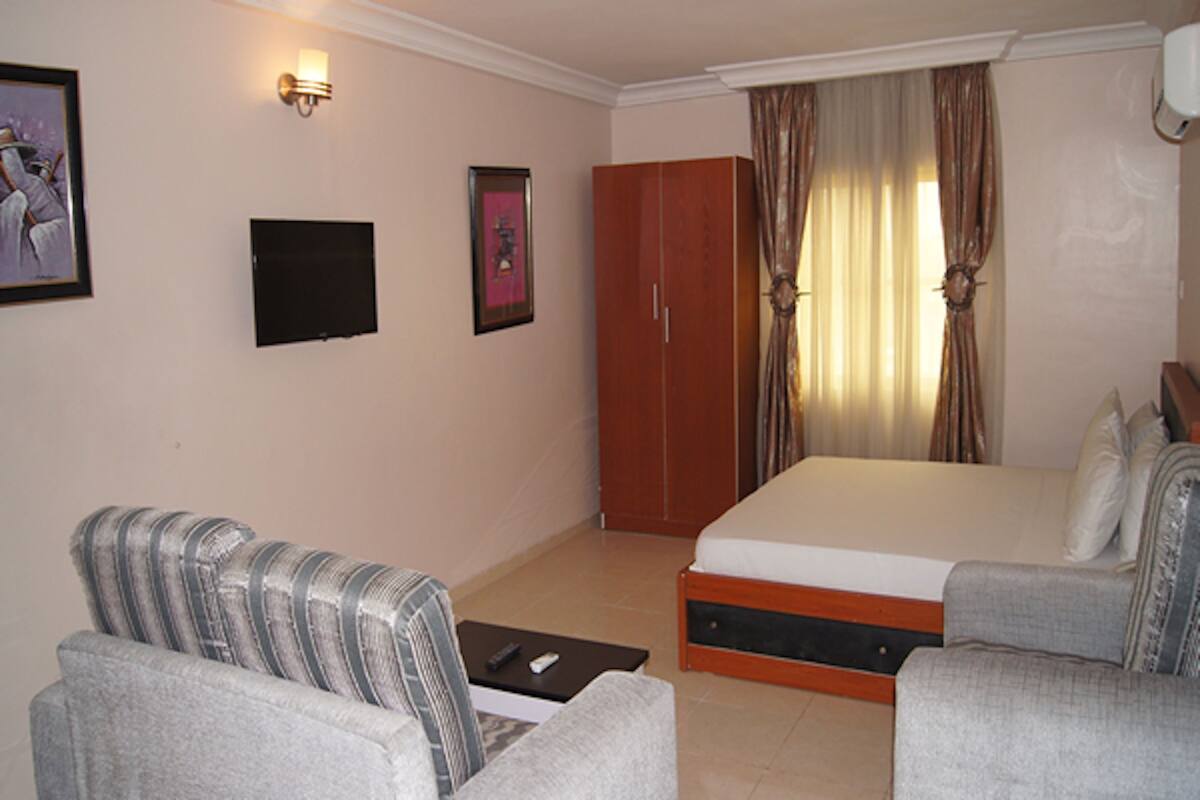 A hotel room with a bed, two armchairs, a TV, and a wardrobe.