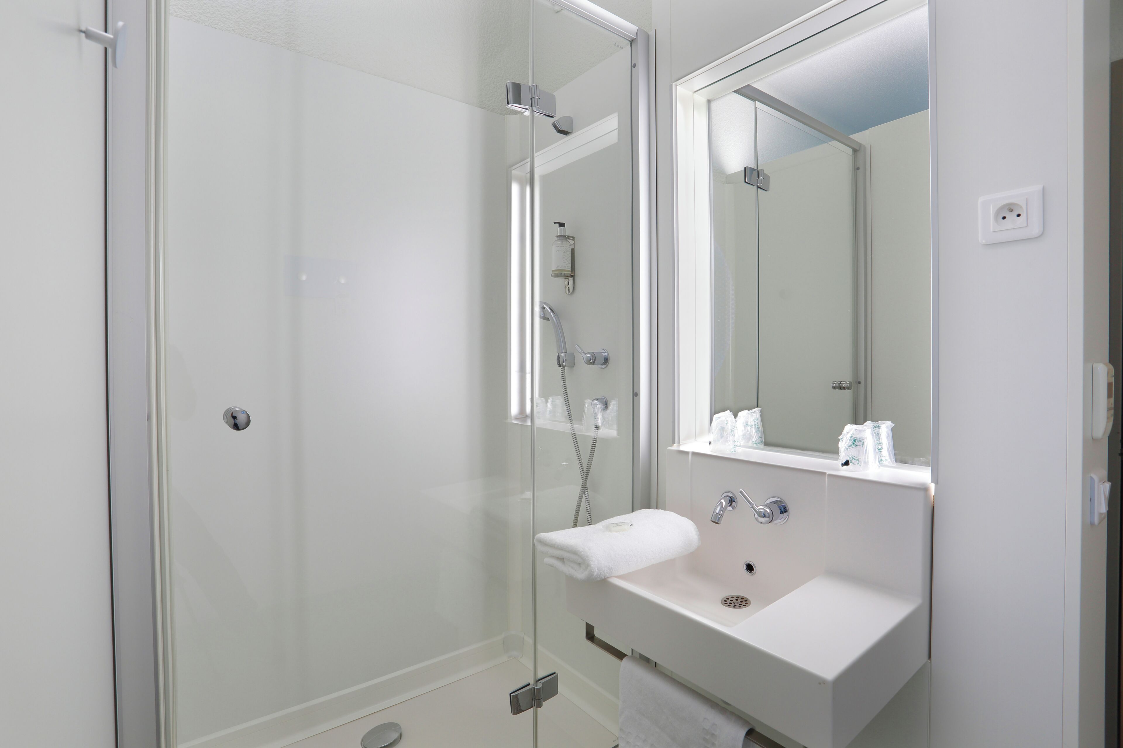 Un baño moderno con ducha de vidrio, lavamanos blanco y un espejo grande.