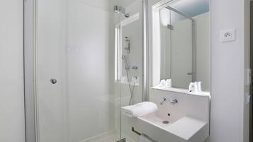 Un baño moderno con ducha de vidrio, lavamanos blanco y un espejo grande.