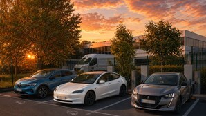 Un parcheggio con tre auto, una recinzione e un edificio sullo sfondo.