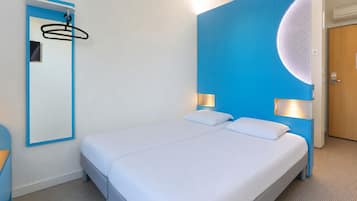 A hotel room with a bed, two bedside lamps, a mirror with a blue frame, and a circular light fixture on the wall.