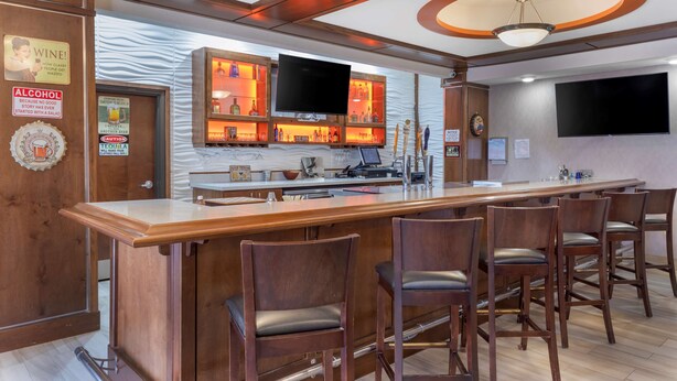 Un espace bar doté d’un long comptoir, de plusieurs tabourets de bar, d’un téléviseur fixé au-dessus du bar, ainsi que de divers panneaux et éléments de décoration sur les murs.