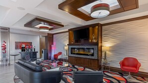 Un hall d’hôtel moderne avec un canapé en cuir noir, un fauteuil rouge, un téléviseur à écran plat et un coin bar.