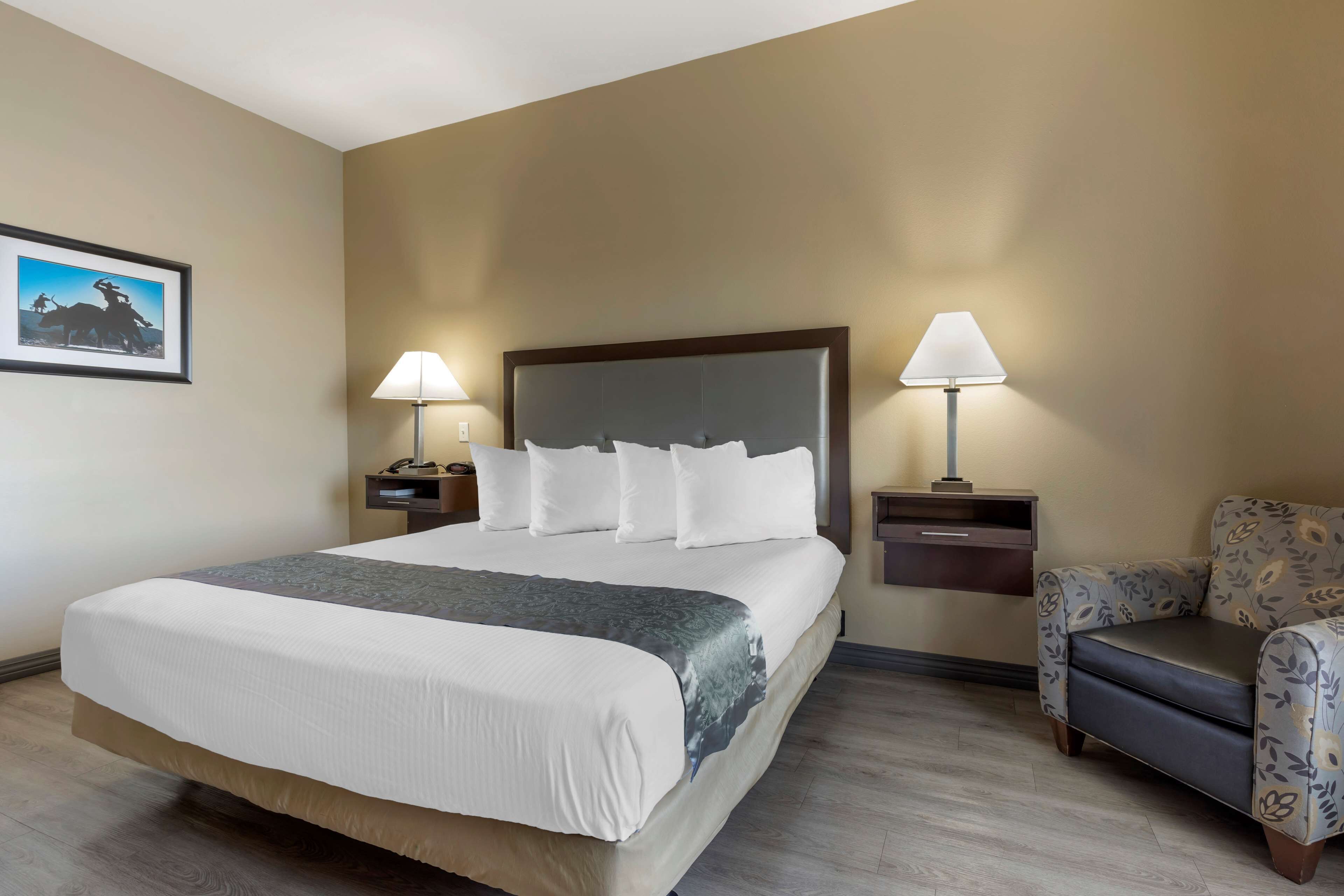 A hotel room with a large bed, two bedside tables with lamps, a chair, and a framed picture on the wall.