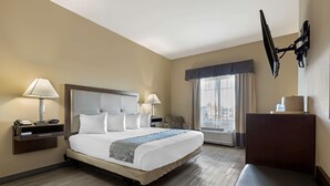 Une chambre d’hôtel avec un grand lit, deux tables de chevet avec des lampes, un téléviseur à écran plat fixé au mur et une fenêtre avec des rideaux.