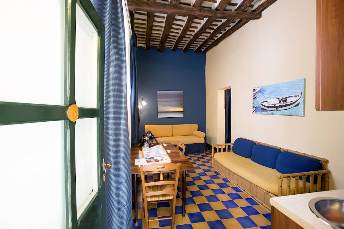 A room with a checkered floor, a wooden table with a menu, a sofa, and a painting of a boat on the wall.
