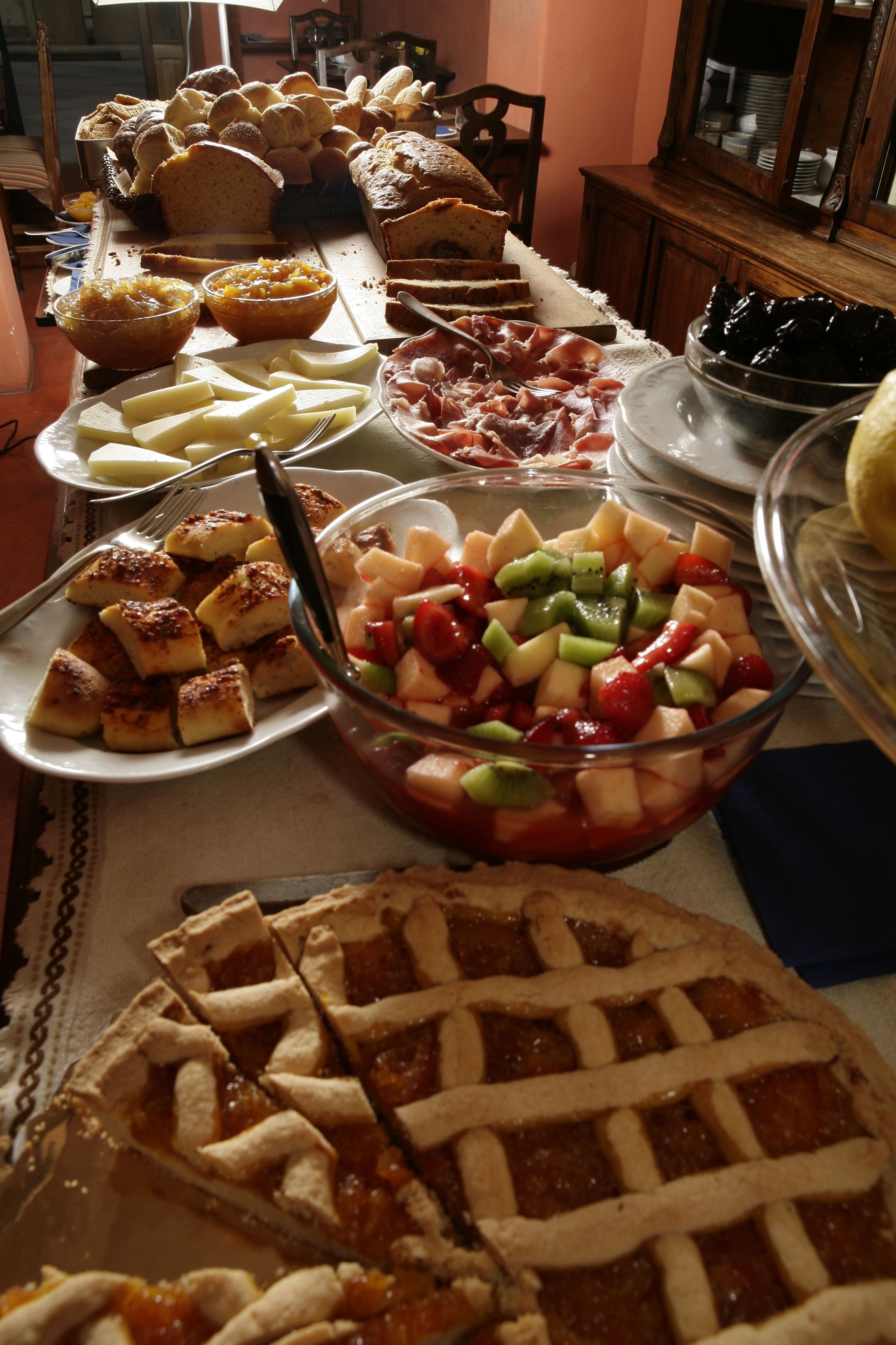 Ein Tisch mit verschiedenen Speisen, darunter Brot, Käse, Schinken und einem Obstsalat.