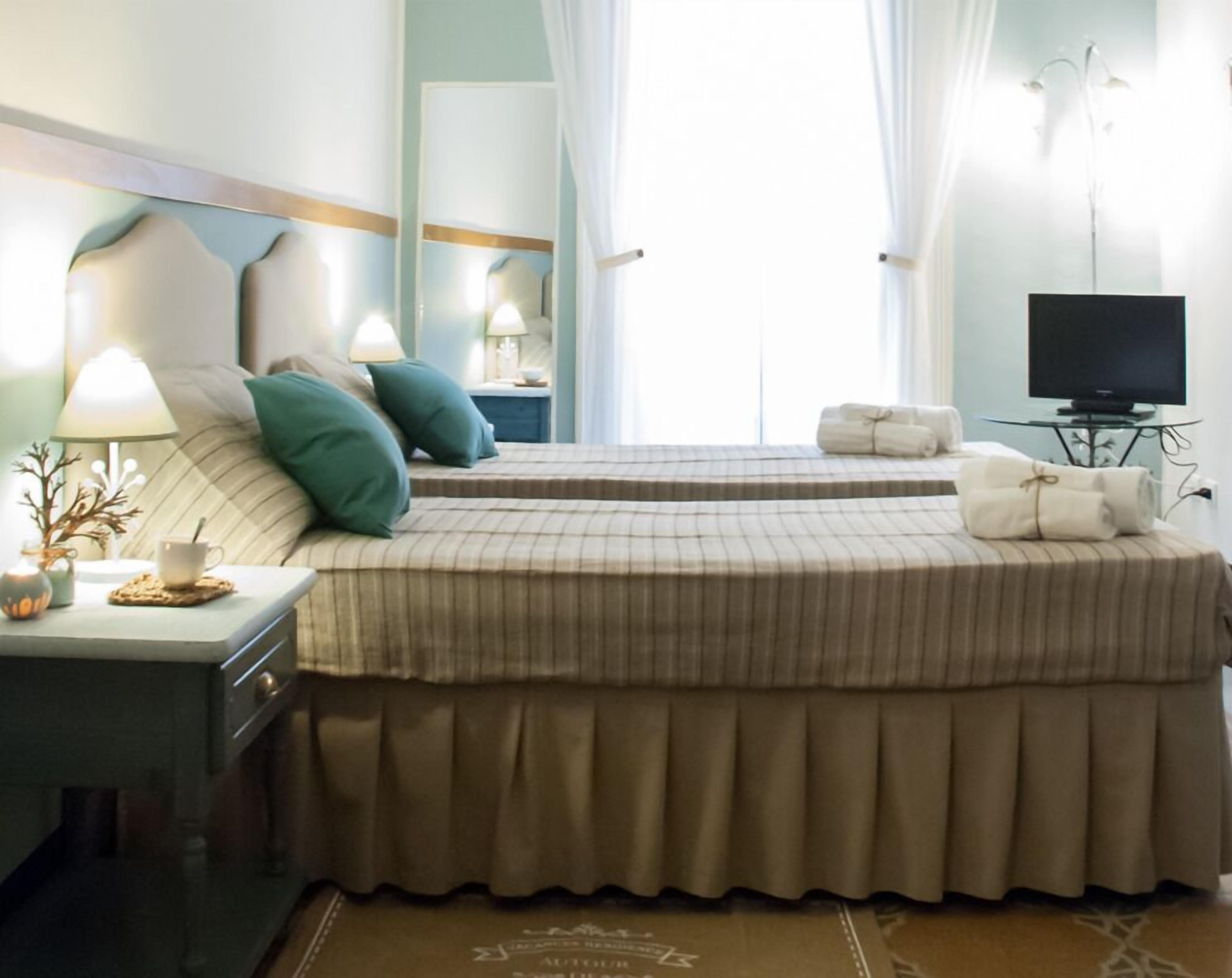 Una camera d'albergo con un letto, un comodino con una lampada, una televisione e una finestra con tende.