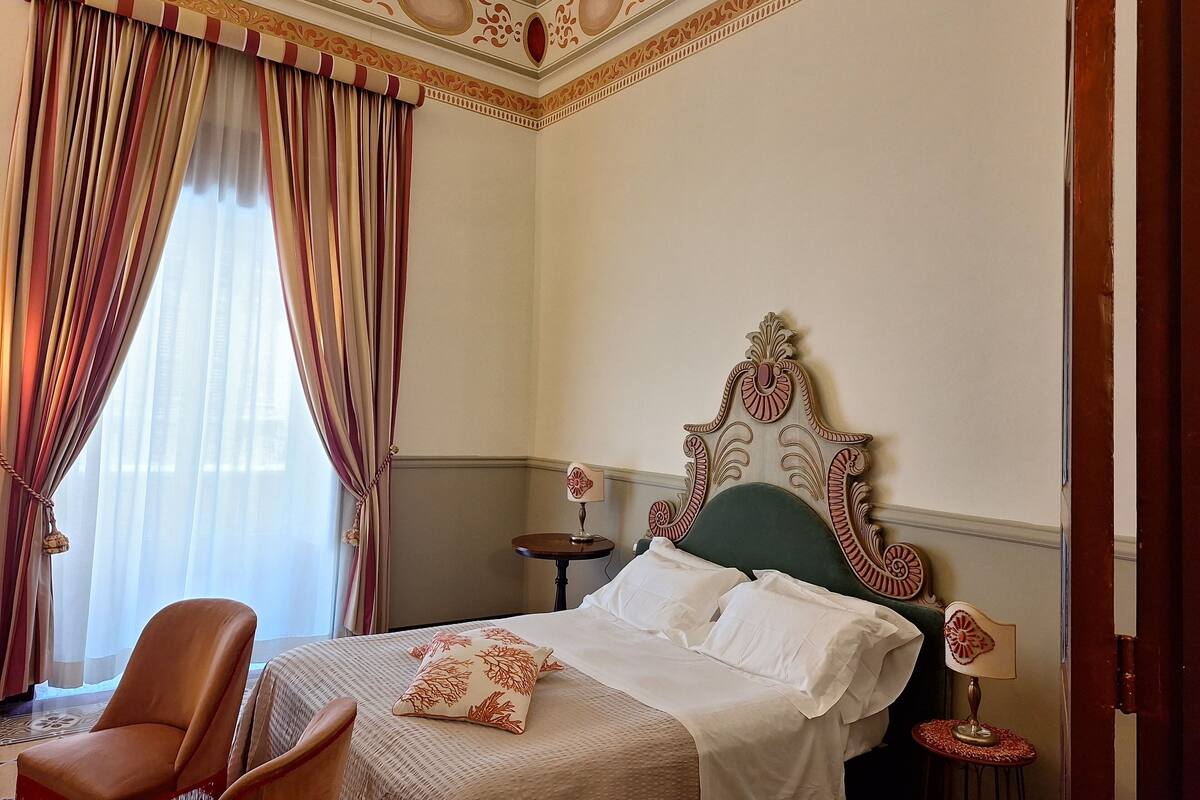 A hotel room with a large bed, a chair, a small table, and a decorative headboard.