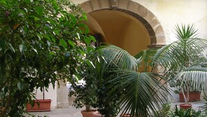 Une cour dotée d’une arche en pierre, de plantes en pot et d’un bâtiment avec des portes et des fenêtres en bois.