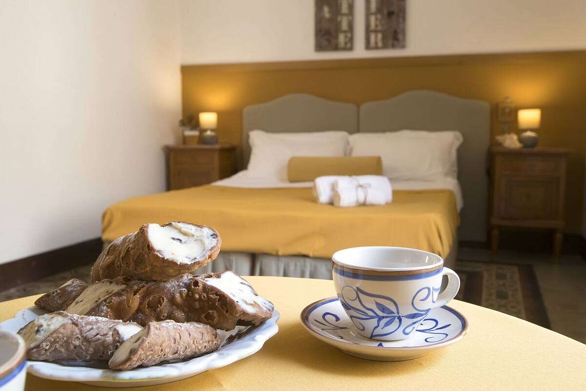 A hotel room with a bed, bedside tables, a plate of pastries, and a cup on a table.