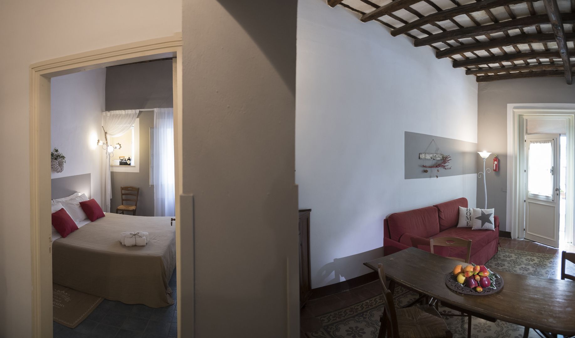 A bedroom with a bed, a chair, and a nightstand. There is a dining area with a table, chairs, and a fruit bowl.