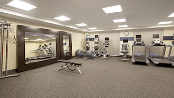 Ein Fitnessraum mit Trainingsgeräten, einem Spiegel und einer Uhr an der Wand.