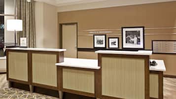 A hotel reception area with a reception desk, a framed welcome sign, and a wall with framed pictures.
