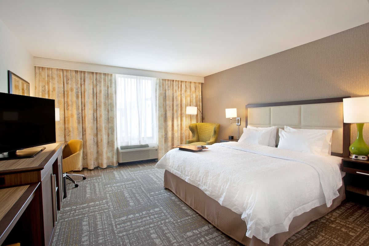 A hotel room with a bed, a desk with a television, a chair, and a lamp.