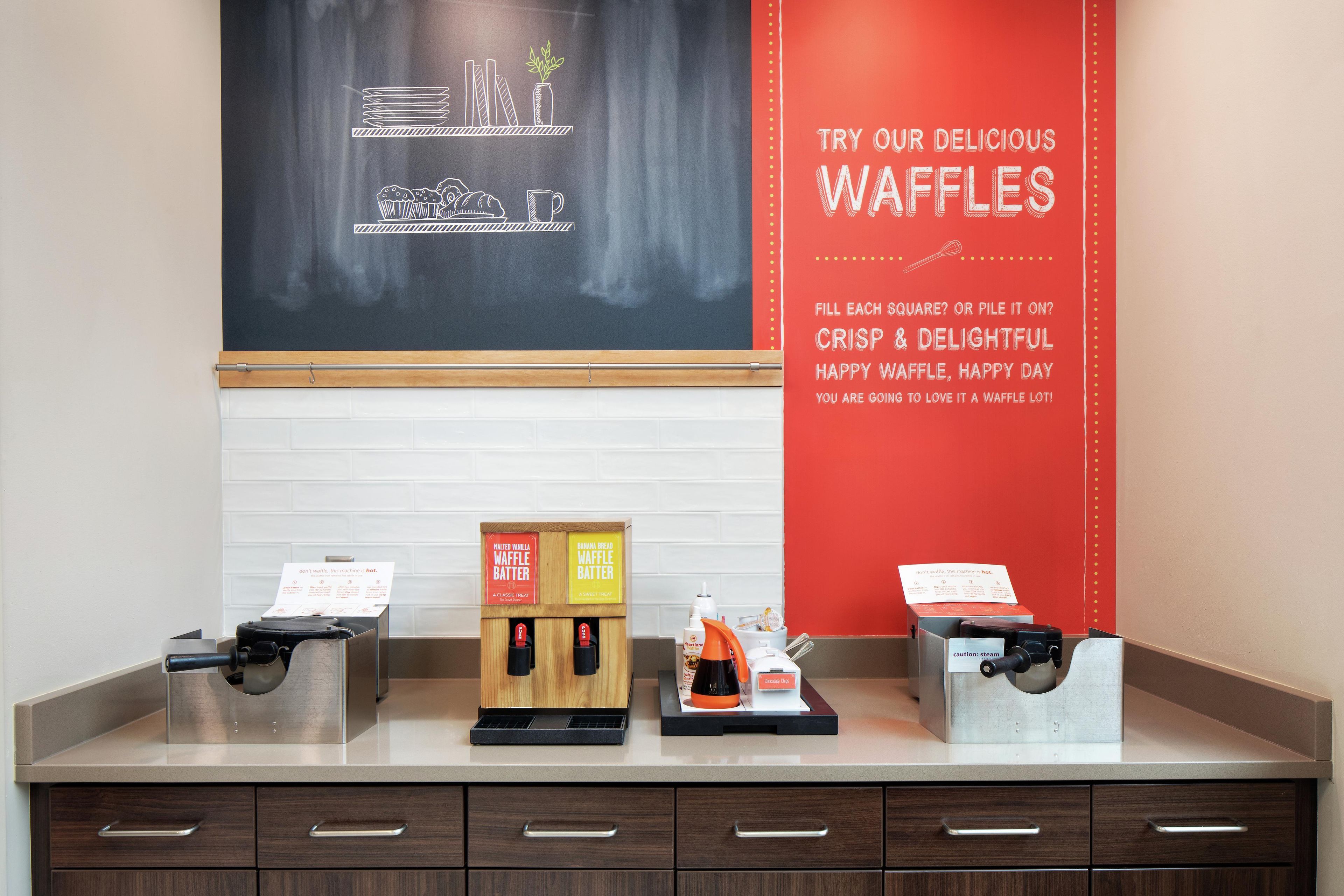 Een wafelstation met twee dispensers voor wafelbeslag en een bord waarop wafels worden aangeboden.