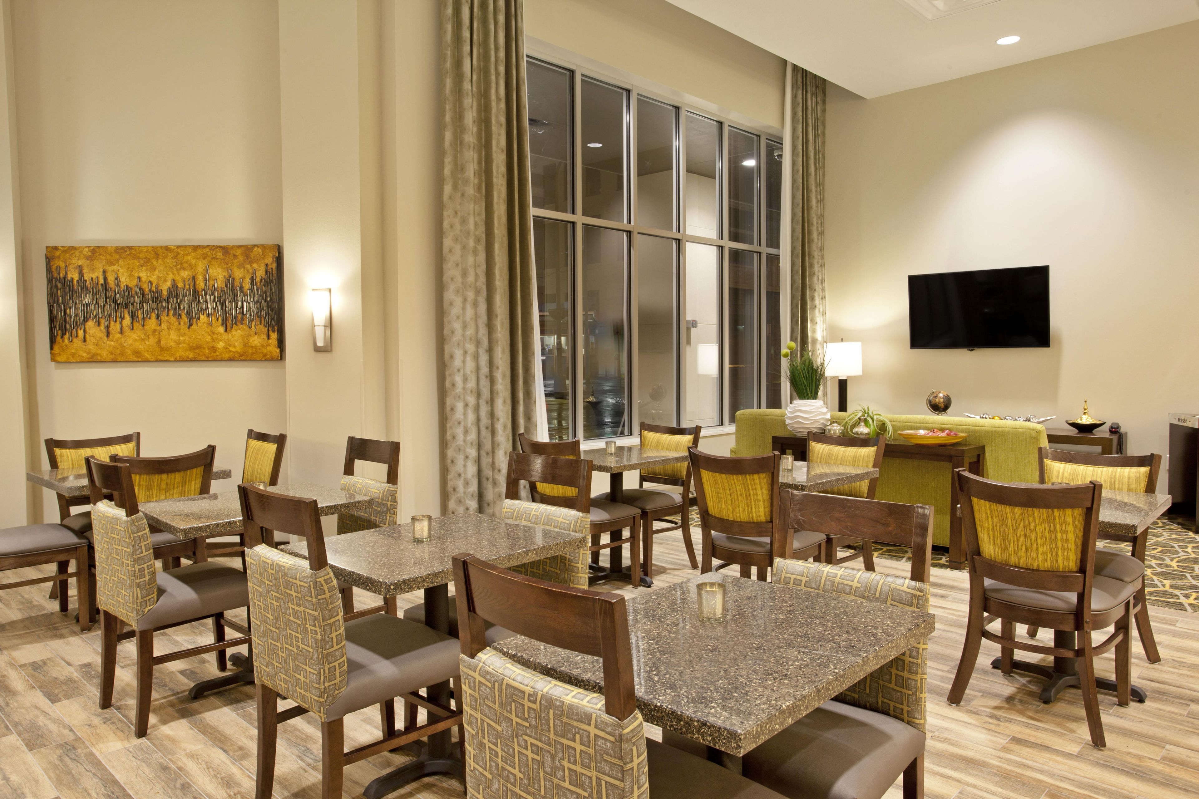 A hotel lobby with a dining area, a flat-screen TV, and a large window.