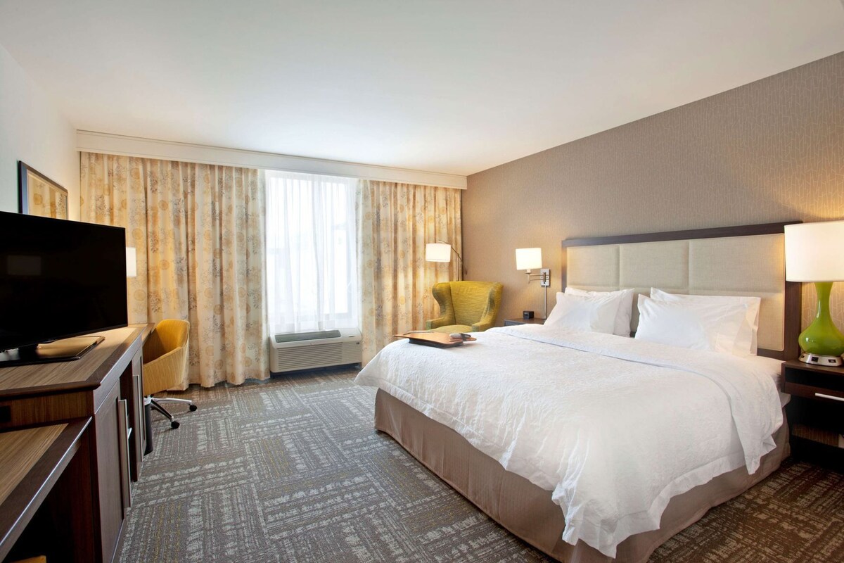 A hotel room with a bed, a television, a chair, a desk, and a window with curtains.