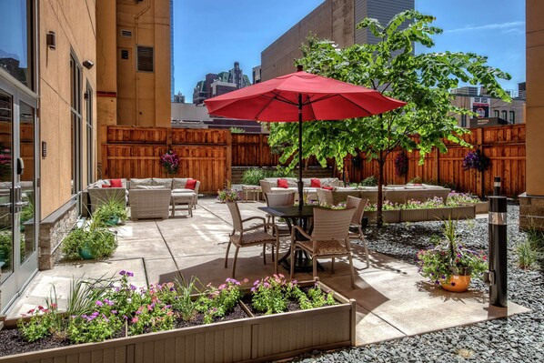 An outdoor patio with wicker furniture, a red umbrella, and potted plants. - Hampton Inn & Suites Minneapolis / Downtown (Minneapolis)