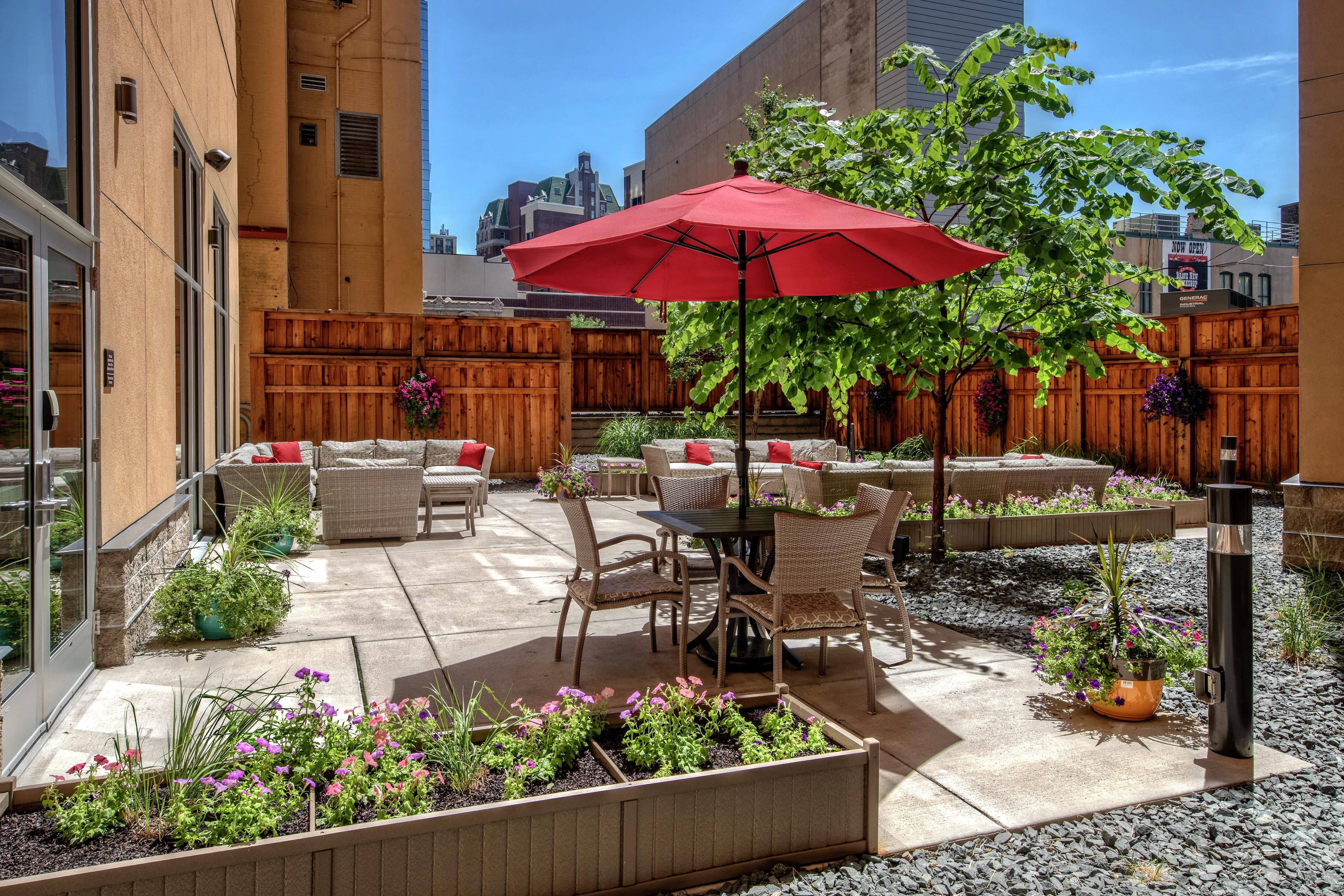 A patio area with outdoor furniture, a red umbrella, and flower beds.