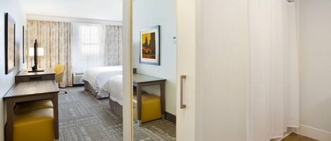 Habitación de hotel con cama, escritorio, silla, espejo y zona de ducha.