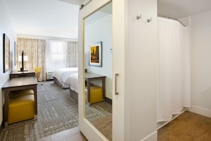A hotel room with a bed, a desk, a chair, a mirror, and a shower area. - Hampton Inn & Suites Minneapolis / Downtown (Minneapolis)