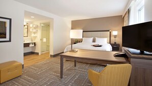 Ein Hotelzimmer mit Bett, Nachttisch, Fernseher, Stuhl und Schreibtisch mit Lampe.