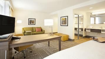 Ein Hotelzimmer mit Bett, Schreibtisch mit Computer, Sofa, Spiegel und Fernseher.