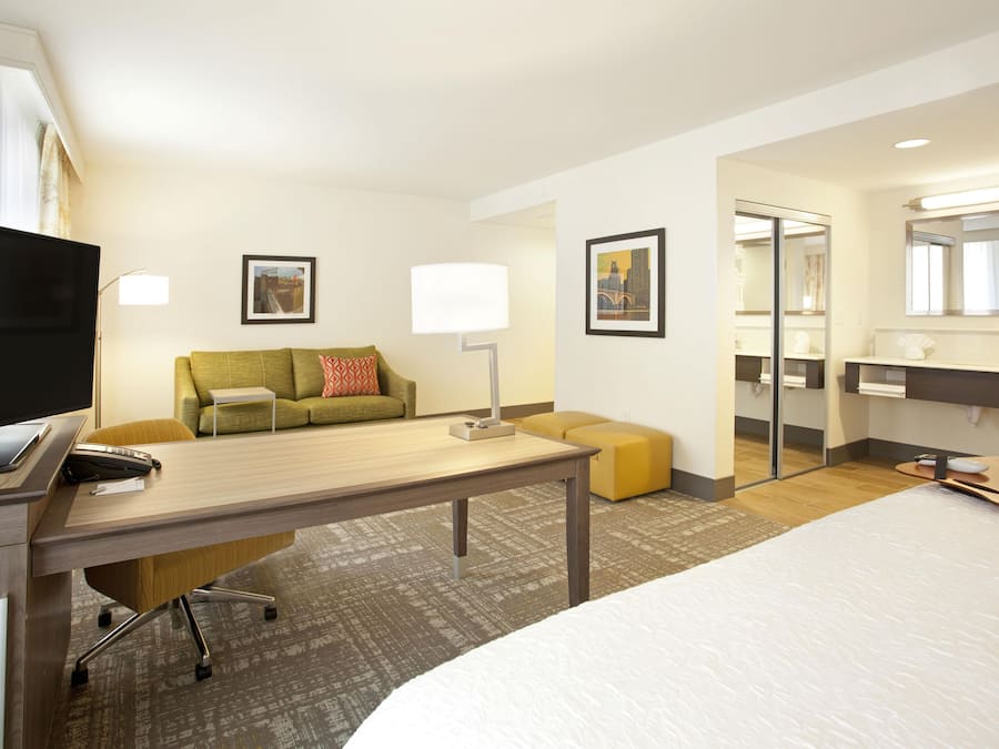 A hotel room with a bed, a desk with a computer, a sofa, a mirror, and a television.