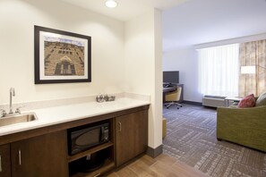 A hotel room with a kitchenette, a desk with a computer, a green sofa, and a large window with curtains. - Hampton Inn & Suites Minneapolis / Downtown (Minneapolis)