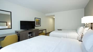 A hotel room with two beds, a desk with a television, a mirror, and a framed picture on the wall.