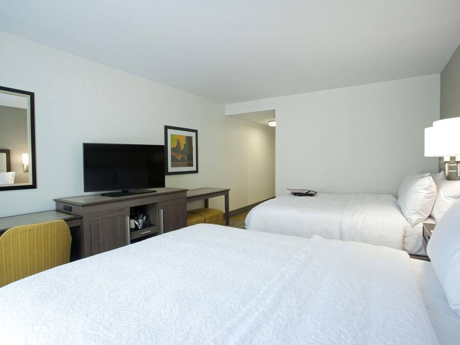 A hotel room with two beds, a desk with a television, a mirror, and a framed picture on the wall.