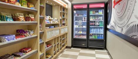 Una sección de aperitivos y bebidas con estantes llenos de diferentes opciones y un congelador exhibiendo postres helados.
