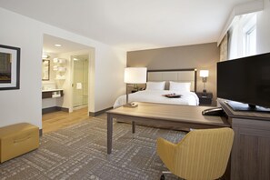 A hotel room with a bed, bedside table, TV, and a seating area with a chair. - Hampton Inn & Suites Minneapolis / Downtown (Minneapolis)