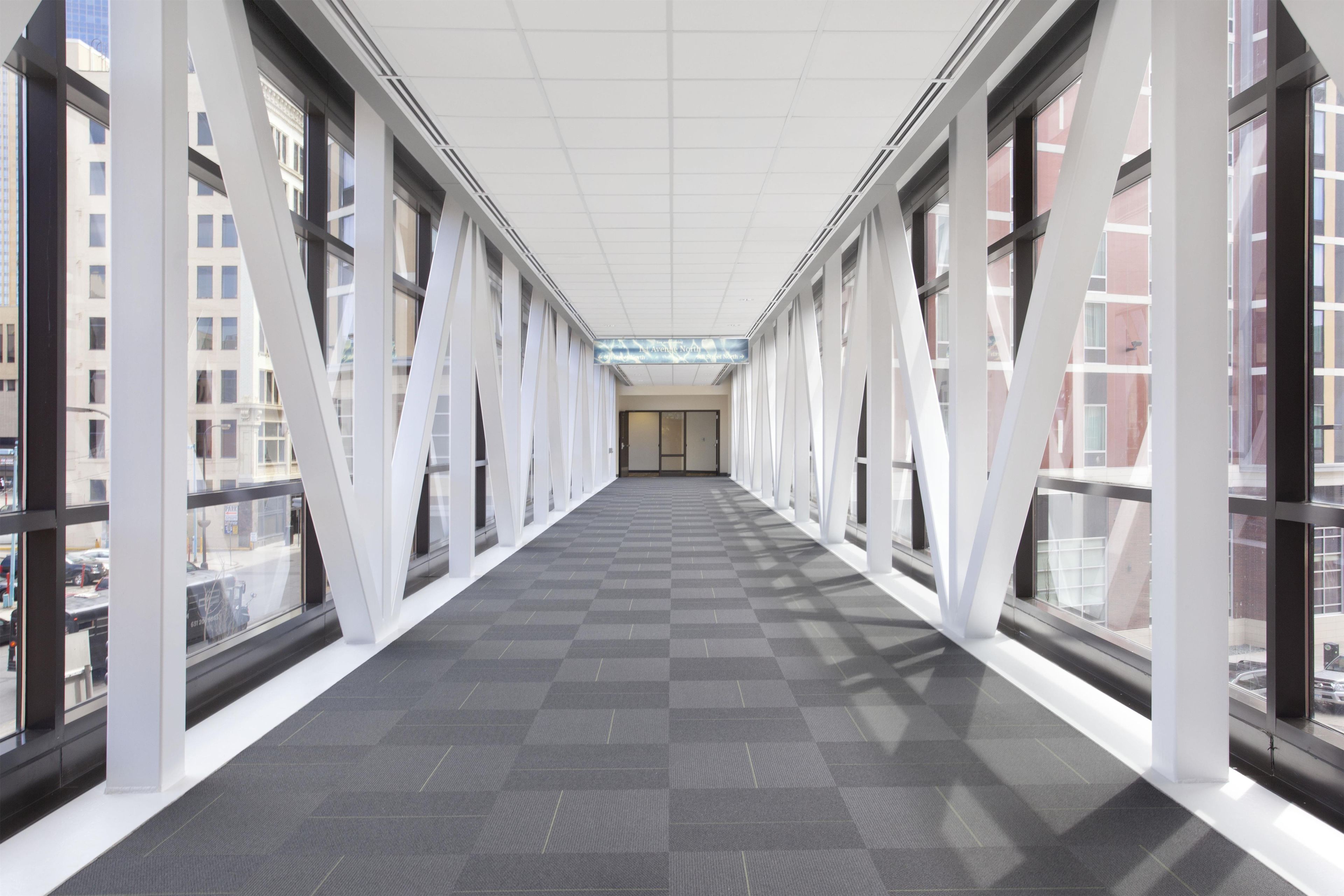 Un couloir doté de grandes fenêtres et d’un sol à carreaux, qui mène à une porte au bout.