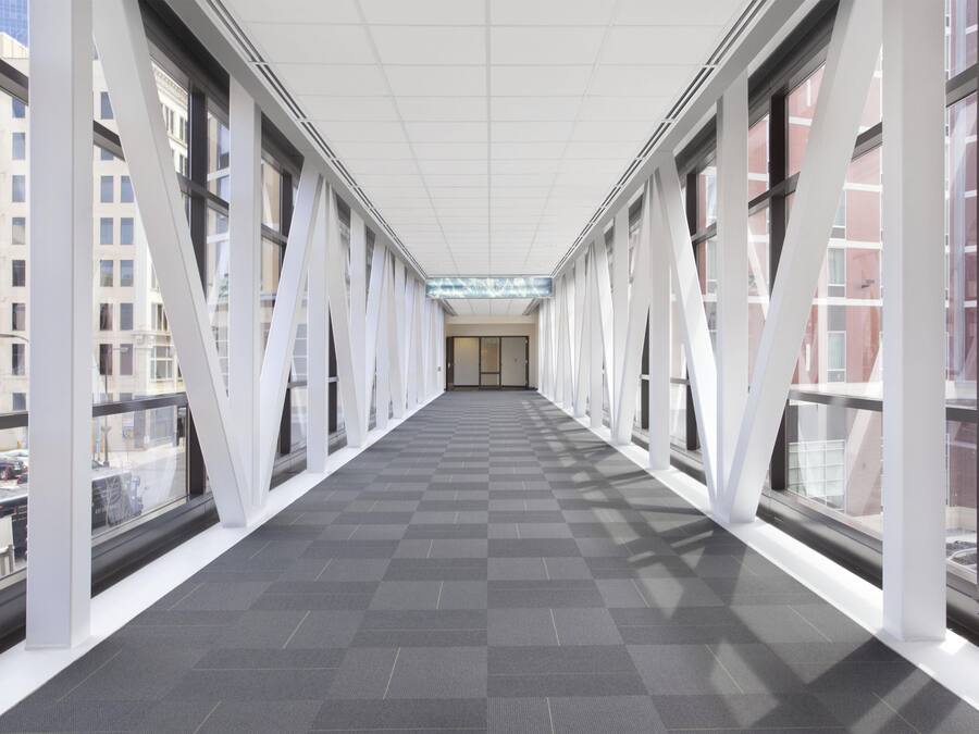 A corridor with large windows and a checkered floor, leading to a door at the end.