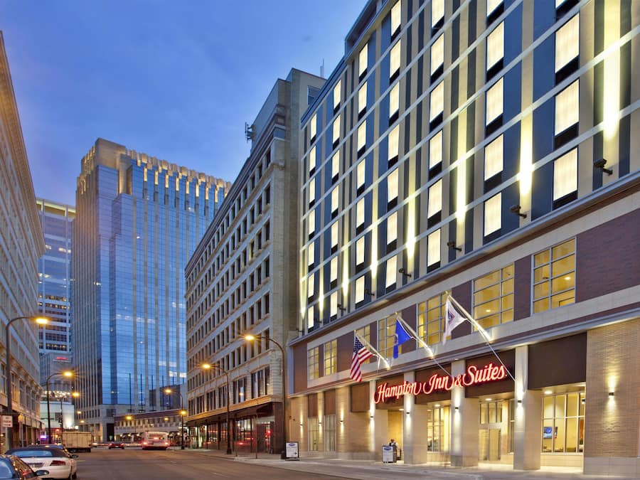 A hotel with a prominent Hampton Inn & Suites sign, large windows, and a modern building facade.